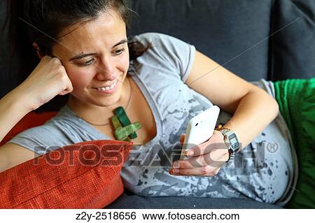 Smily woman on a pillow holding her head and checking her phone. View Large Photo Image Stock Photograph - Smily woman on a pillow holding her head and checking her phone.. Fotosearch