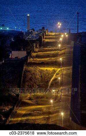 Sodium vapor lights illuminate the hilly international border between the U. S. and Tijuana, Mexico at left. Note Pacific Ocean and lighthouse in background. View Large Photo Image Stock Photo - Sodium vapor lights illuminate the hilly international border between the U. S. and Tijuana, Mexico at left. Note Pacific Ocean and lighthouse in background.. Fotosearch