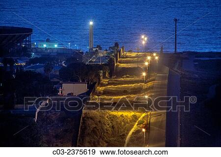 Sodium vapor lights illuminate the hilly international border between the U. S. and Tijuana, Mexico at left. Note Pacific Ocean and lighthouse in background. View Large Photo Image Stock Photo - Sodium vapor lights illuminate the hilly international border between the U. S. and Tijuana, Mexico at left. Note Pacific Ocean and lighthouse in background.. Fotosearch