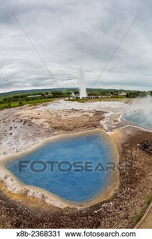 Strokkur geyser erupting behind hot springs in the Haukadalur valley on the slopes of Laugarfjall hill, near the Hv? tß River, Iceland. View Large Photo Image Stock Image - Strokkur geyser erupting behind hot springs in the Haukadalur valley on the slopes of Laugarfjall hill, near the Hv? tß River, Iceland.. Fotosearch