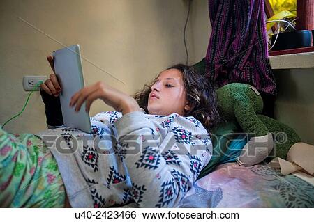 Stock Photograph - Teenage girl in bed on iPad.. Fotosearch