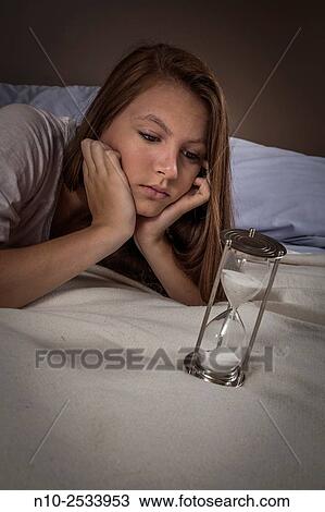 Stock Image - Teenage girl on her bed with an hourglass.. Fotosearch