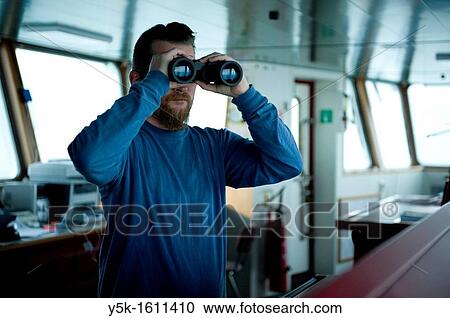 The captain of the container-vessel MV Flintercape uses binoculars to spot for other ships in the vicinity, during the voyage from Rotterdam, Netherlands to Sundsvall, Sweden. View Large Photo Image Stock Image - The captain of the container-vessel MV Flintercape uses binoculars to spot for other ships in the vicinity, during the voyage from Rotterdam, Netherlands to Sundsvall, Sweden.. Fotosearch