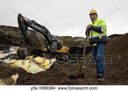 Picture - This 67-year old man still works as a freelance machinist on an excavator on top of the regional dump-site near Tilburg, The Netherlands. He does his job full of joy!. Fotosearch