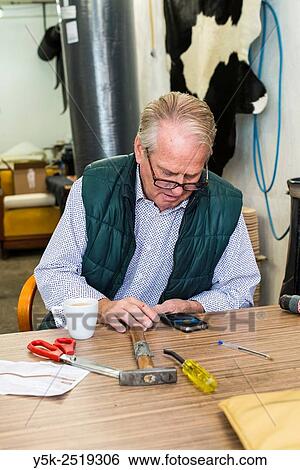 Tilburg, Netherlands. The 72 year old upholsterer Boy, reading the messages on his smartphone, while sitting at his workbench. View Large Photo Image Stock Photograph - Tilburg, Netherlands. The 72 year old upholsterer Boy, reading the messages on his smartphone, while sitting at his workbench.. Fotosearch