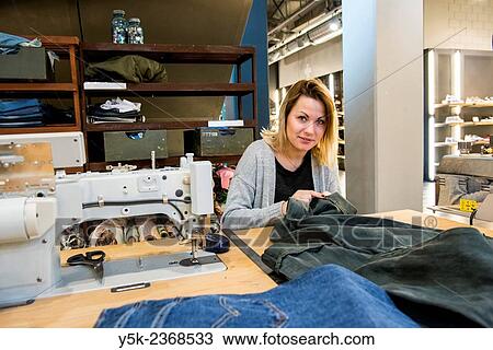 Tilburg, Netherlands. Young needlewoman buzzy shortening a jeans at her workstation in a fashion store for one of her customers. View Large Photo Image Stock Image - Tilburg, Netherlands. Young needlewoman buzzy shortening a jeans at her workstation in a fashion store for one of her customers.. Fotosearch