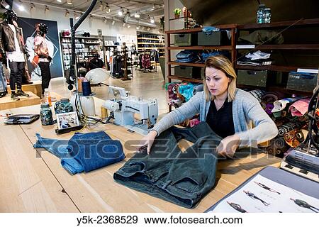 Tilburg, Netherlands. Young needlewoman preparing to shorten a jeans at her workstation in a fashion store for one of her customers. View Large Photo Image Stock Photo - Tilburg, Netherlands. Young needlewoman preparing to shorten a jeans at her workstation in a fashion store for one of her customers.. Fotosearch