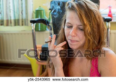 Tilburg, Netherlands. Young woman wearing just a shirt smoking a cigarillo, while sitting down in a living room. View Large Photo Image Stock Photography - Tilburg, Netherlands. Young woman wearing just a shirt smoking a cigarillo, while sitting down in a living room.. Fotosearch
