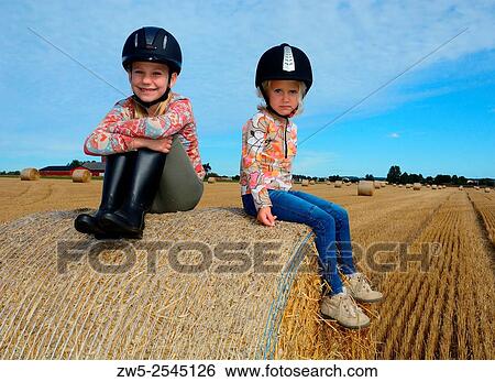 Two girls, 9 and 4 years old, sit on a straw bale at a field in Scania, Sweden. View Large Photo Image Stock Photograph - Two girls, 9 and 4 years old, sit on a straw bale at a field in Scania, Sweden.. Fotosearch