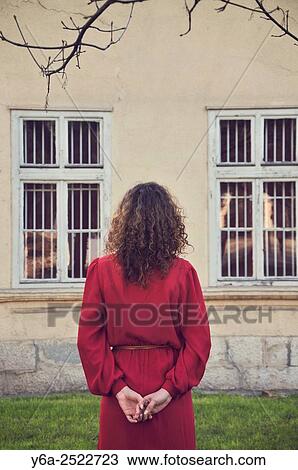 Stock Image - Woman in red dress standing outdoors, rear view.. Fotosearch