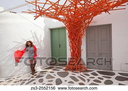 Stock Photograph - Woman posing with an orange scarf near a whitewashed house in town center, Mykonos, Cyclades Islands, Greek Islands, Greece, Europe.. Fotosearch