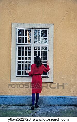 Stock Photograph - Woman standing outside the house looking through window.. Fotosearch