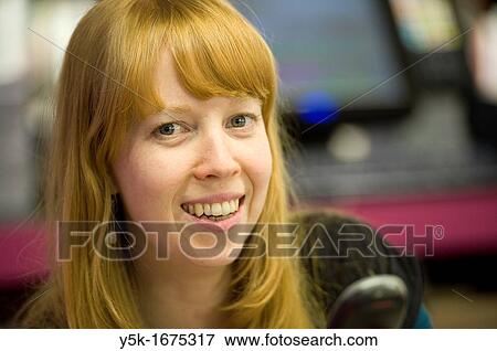 Stock Photo - Young, attractive and redheaded woman, working full of joy, in a museum bookstore.. Fotosearch
