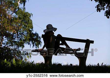 Stock Photograph - Young female on bench silhouetting against Blue sky. Fotosearch