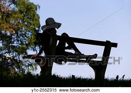 Stock Photography - Young female on bench silhouetting against Blue sky. Fotosearch