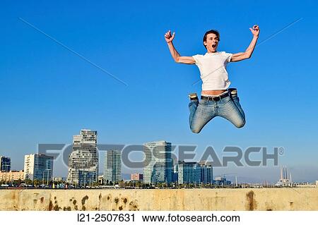 Stock Image - Young man jumping against city skyline. Barcelona, Catalonia, Spain.. Fotosearch