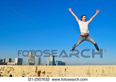 Stock Image - Young man jumping against city skyline. Barcelona, Catalonia, Spain.. Fotosearch