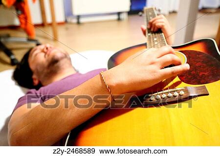 Stock Photo - Young man laying on the ground and playing guitar.. Fotosearch