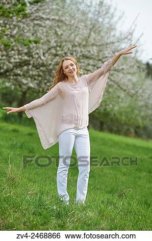 Stock Photograph - Young woman between flowering apple trees in spring.. Fotosearch