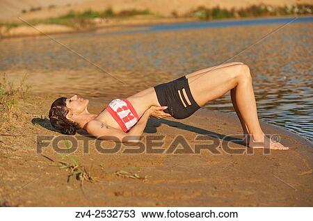 Stock Image - Young woman doing yoga on a beach next to a little lake.. Fotosearch