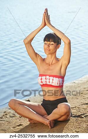 Stock Photography - Young woman doing yoga on a beach next to a little lake.. Fotosearch