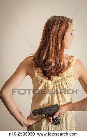 Stock Image - Young woman holding a gun behind her back.. Fotosearch