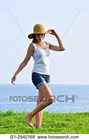 Young woman in summer clothes and straw hat standing on the grass near the sea. She is dressed with short jeans and a white blouse. View Large Photo Image Stock Photo - Young woman in summer clothes and straw hat standing on the grass near the sea. She is dressed with short jeans and a white blouse.. Fotosearch