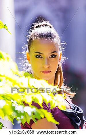 Stock Photo - Young woman portrait behind bright leaves.. Fotosearch