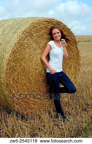 Stock Photo - Young woman standing at a round bale of straw in Scania, Sweden.. Fotosearch