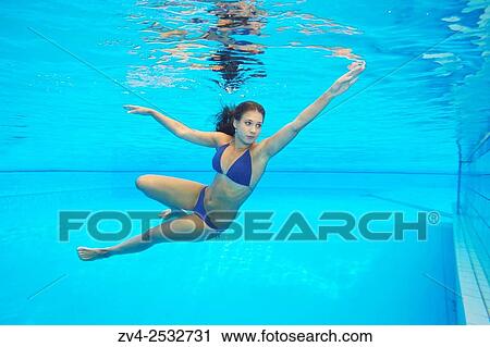 Stock Image - Young woman wearing a bikini while swimming under water in a open-air pool.. Fotosearch