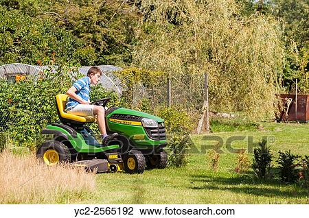 Stock Image - A 15 year old boy mowing the lawn on a John Deere ride on mower in the Uk.. Fotosearch