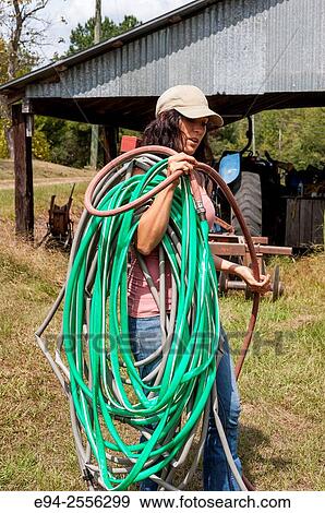 A 38 year old brunette woman working outdoors on a farm carrying a bunch of garden hose on her shoulder. View Large Photo Image Stock Photo - A 38 year old brunette woman working outdoors on a farm carrying a bunch of garden hose on her shoulder.. Fotosearch