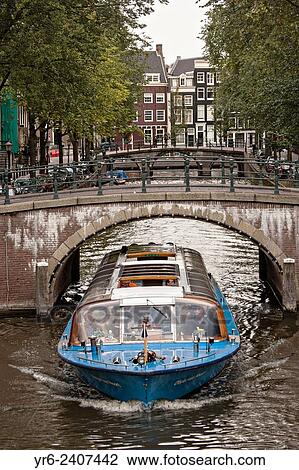Stock Image - A tour boat passes under the Hemonybrug bridge at Keizersgracht and Leidsegracht in Amsterdam.. Fotosearch