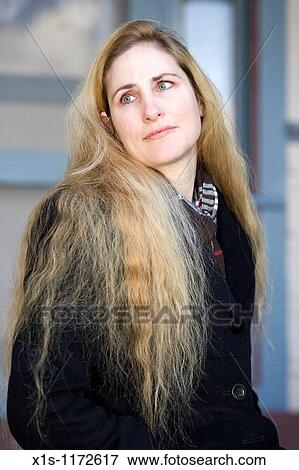 A woman with long blond hair sitting outside wearing a coat and looking off over one shoulder. View Large Photo Image Stock Photo - A woman with long blond hair sitting outside wearing a coat and looking off over one shoulder.. Fotosearch