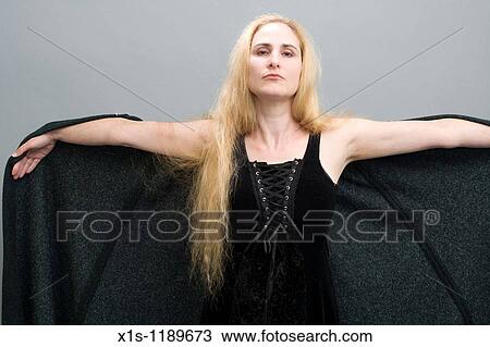 Stock Image - An attractive American woman with beautiful long, flowing blond hair extends a black cape out from both arms.. Fotosearch