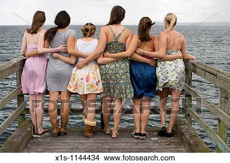 At the end of a pier, six young women with their backs to the camera are connected by arms as they look out into the water View Large Photo Image Picture - At the end of a pier, six young women with their backs to the camera are connected by arms as they look out into the water. Fotosearch
