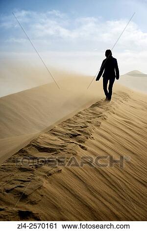 Stock Image - China, Gansu Province, Dunhuang, Crescent Lake (Yueyaquan), woman in the desert walking on the crest of a frozen sand dune, Model Released.. Fotosearch