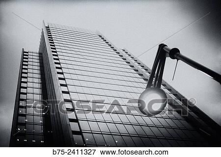 Stock Photo - Closeup of a lighted lamp and an office skyscraper in the background in Canary Wharf, London, England, UK, Europe.. Fotosearch