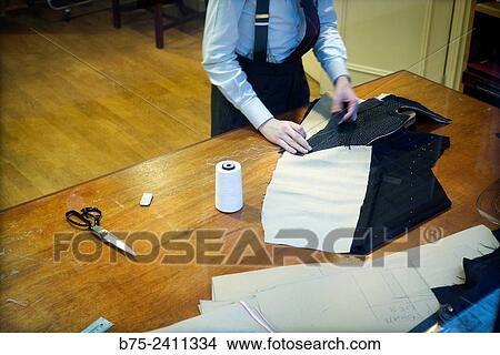 Picture - Closeup of an unrecognizable Tailor, sewing a suit at his desk, scissors, thread, chalk and patterns. Savile Row, London, England, UK, Europe.. Fotosearch
