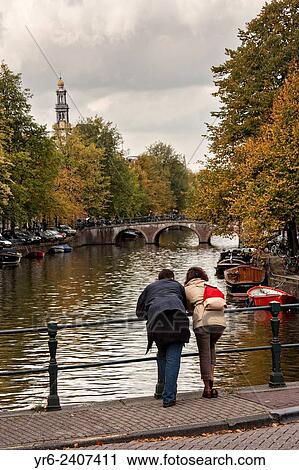 Couple looks at the canal along Prinsengracht with the Westerkerk tower during autumn in Amsterdam. View Large Photo Image Stock Image - Couple looks at the canal along Prinsengracht with the Westerkerk tower during autumn in Amsterdam.. Fotosearch