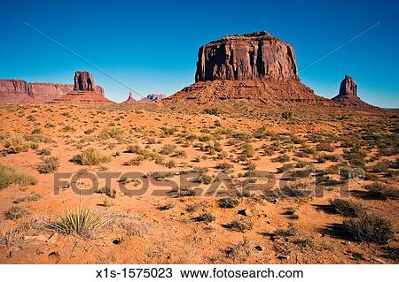 Stock Image - Desert vegetation and sage brush pot mark the desert landscape leading to the iconic rock formations in Monument Valley on a bright sunny day without a cloud in the sky.. Fotosearch