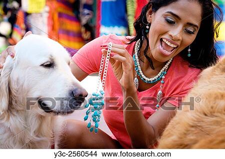 Hispanic woman trying on jewelry while playing with dogs at a street market in Puerto Vallarta, Mexico. View Large Photo Image Picture - Hispanic woman trying on jewelry while playing with dogs at a street market in Puerto Vallarta, Mexico.. Fotosearch
