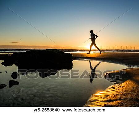 Stock Image - Jogger on beach at sunrise. Seaton Carew, England, United Kingdom.. Fotosearch