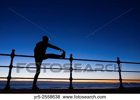 Stock Photo - Jogger stretching in pre dawn light with Venus shining bright on the first day of Autumn at Seaton Carew on the north east coast of England. United Kingdom.. Fotosearch