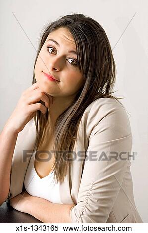 Long haired girl in beige sweater and white shirt rests her chin on her hand as she leans forward while seated. View Large Photo Image Stock Photography - Long haired girl in beige sweater and white shirt rests her chin on her hand as she leans forward while seated.. Fotosearch