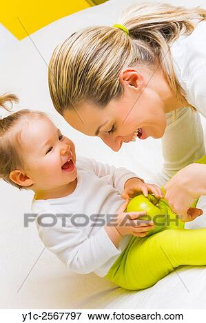 Stock Photo - Mather and baby together with green apple in hands. Fotosearch