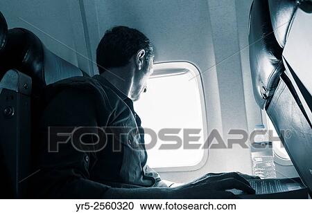 Stock Image - Mature man looking out of airplane window.. Fotosearch