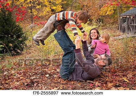 Nuclear family with parents in their 30s and with a 3 year old boy and a one year old girl playing on leaf covered lawn in fall, with a garden shed in their backyard behind them. View Large Photo Image Stock Photo - Nuclear family with parents in their 30s and with a 3 year old boy and a one year old girl playing on leaf covered lawn in fall, with a garden shed in their backyard behind them.. Fotosearch