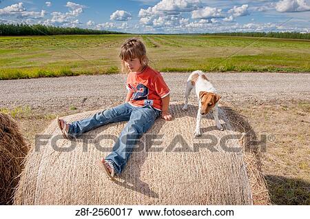 Stock Photo - Portrait of a little girl sitting on a bale of hay with her dog.. Fotosearch