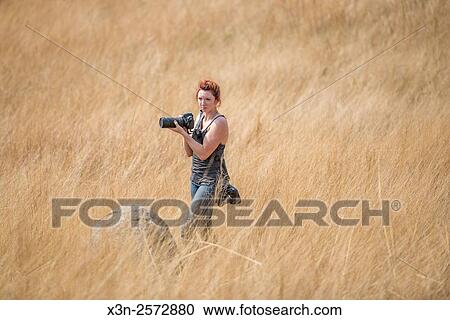 Stock Image - Red head girl standing with cameras in the middle of a field at Mlilwane Wildlife Sanctuary in Swaziland, Africa.. Fotosearch